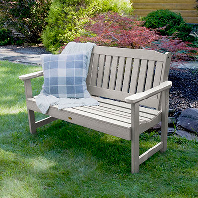 Light gray 4ft Lehigh garden bench with pillow and blanket in grassy area.