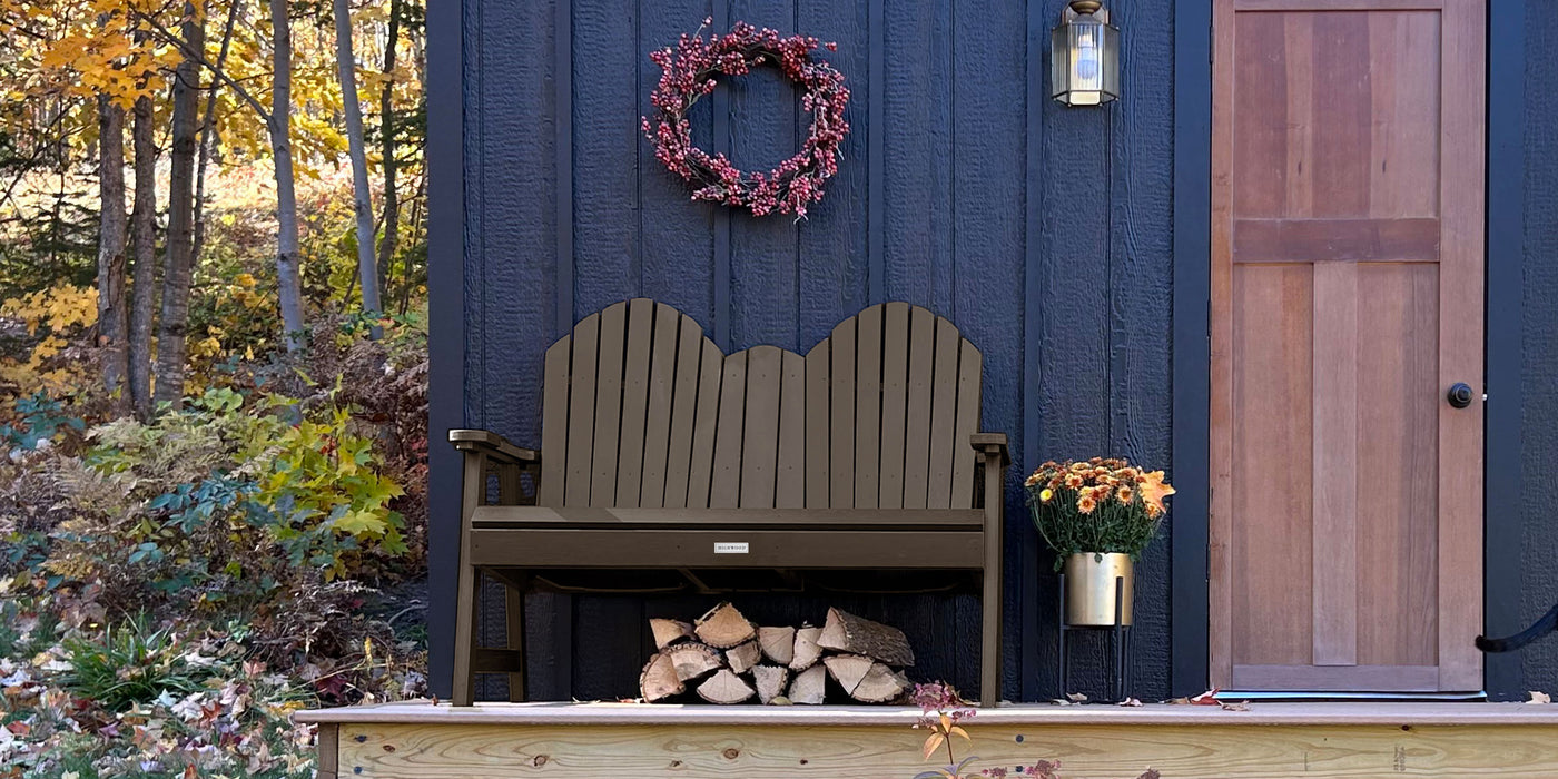 Outdoor bench with firewood against a blue wall with a wreath, in front of a wooden door.