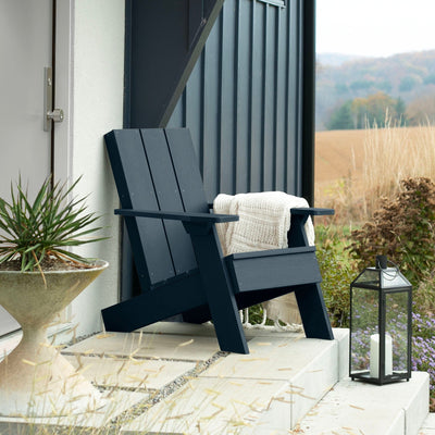 Dark blue Italica Modern Adirondack chair on porch with blanket and lantern