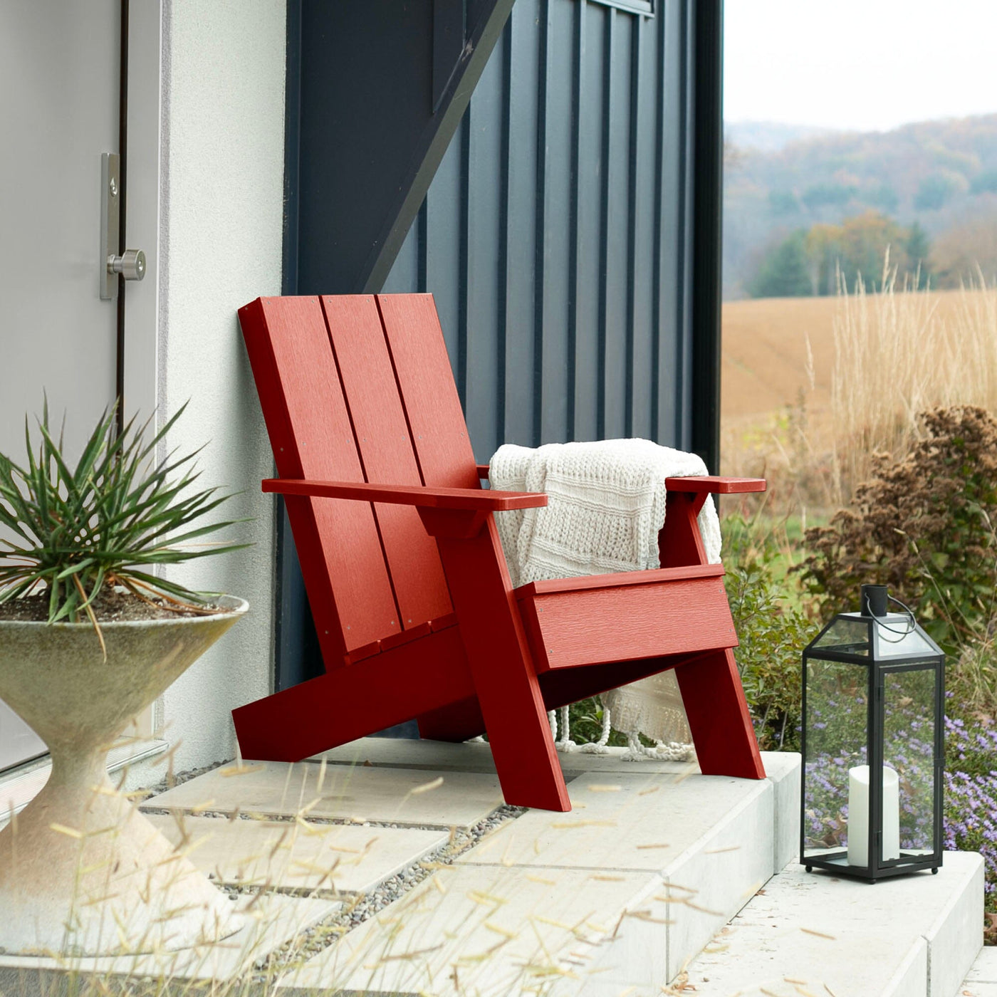 Red Italica Modern Adirondack chair on porch with blanket and lantern