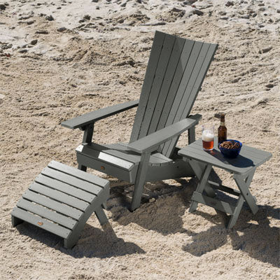 Light gray Manhattan Beach Adirondack chair, ottoman, and folding side table on a beach. 
