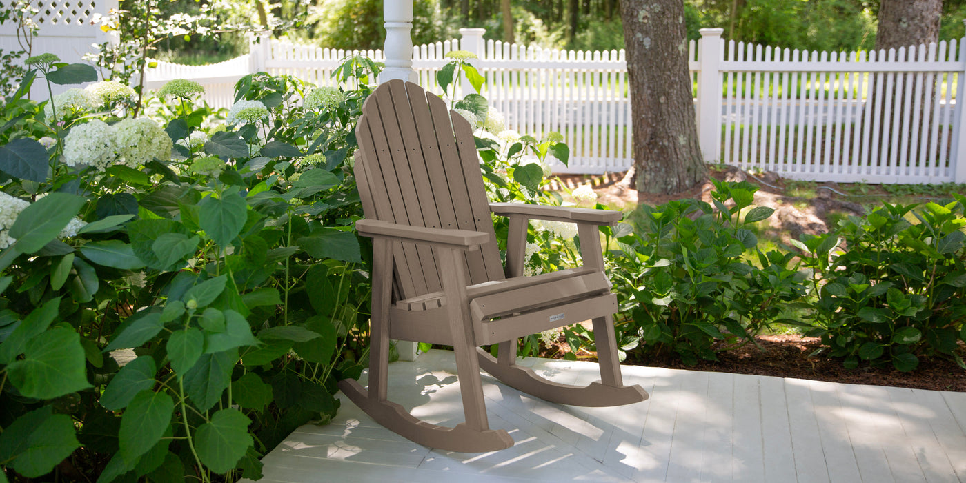 Poly lumber rocking chair on a porch with greenery and a white picket fence in the background