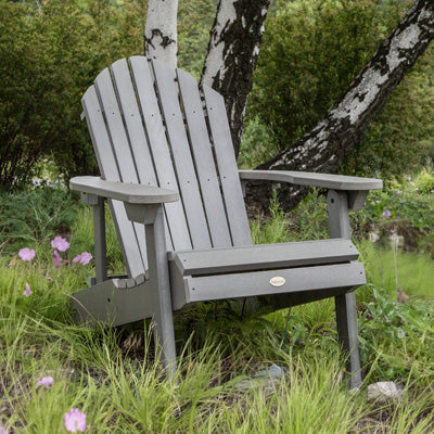 Gray Hamilton Adirondack chair on grass with purple flowers. 