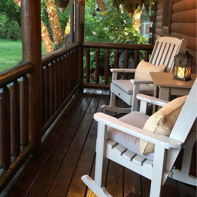 Two white Lehigh rocking chairs with cushions and pillows on brown porch. 