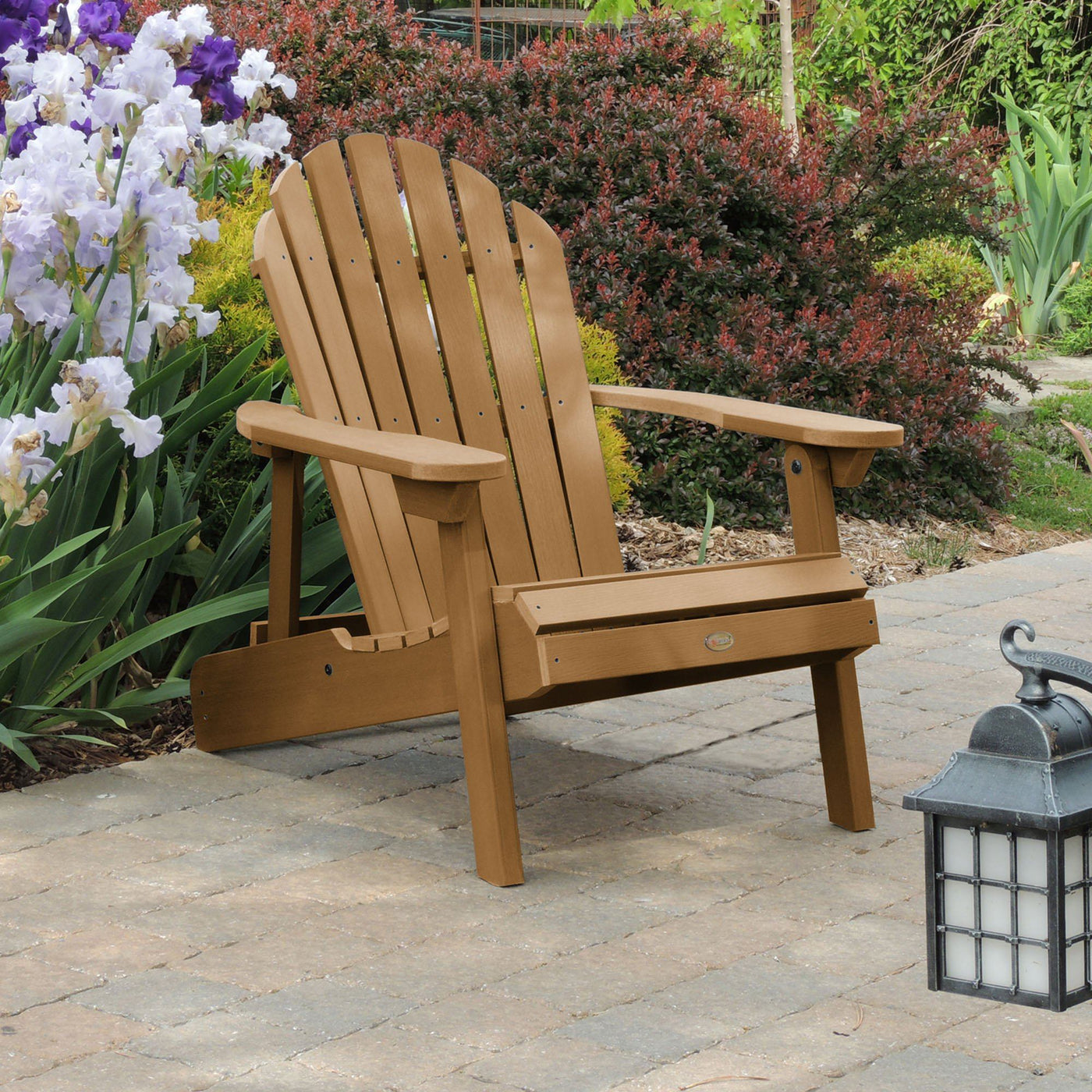Toffee brown Hamilton Adirondack chair on stone with flowers behind