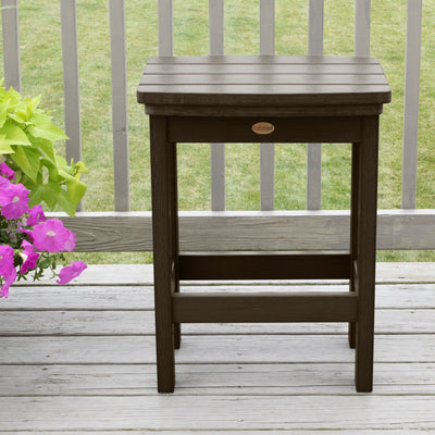 Brown Lehigh counter height stool on deck with flowers in background