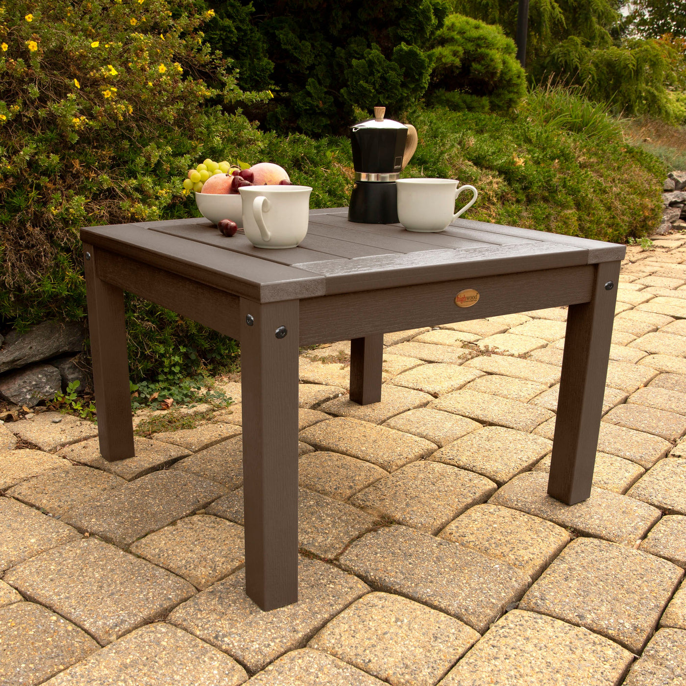 Brown outdoor table on a stone patio with fruits and coffee setup